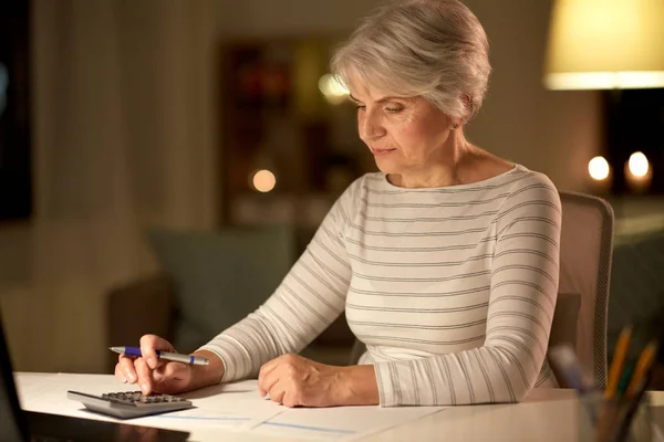 Mulher velha contando com calculadora em casa à noite — Fotografia de Stock