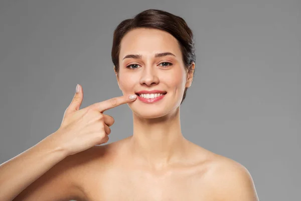 Uśmiechnięta młoda kobieta wskazująca na jej usta — Zdjęcie stockowe