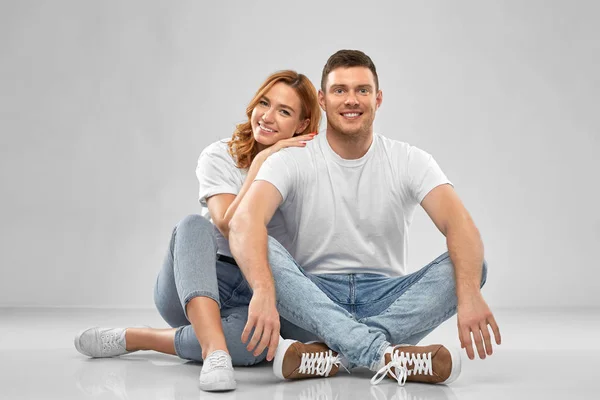 Ευτυχισμένο ζευγάρι με λευκά μπλουζάκια που κάθονται στο πάτωμα — Φωτογραφία Αρχείου