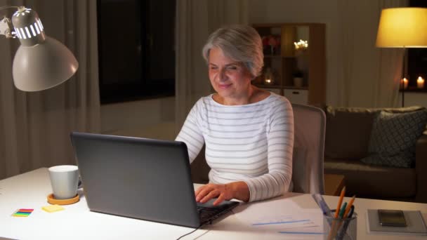 Akşam evde dizüstü bilgisayarı olan mutlu bir yaşlı kadın. — Stok video