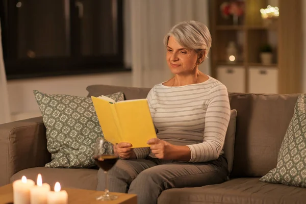 Wanita senior yang bahagia membaca buku di rumah di malam hari — Stok Foto