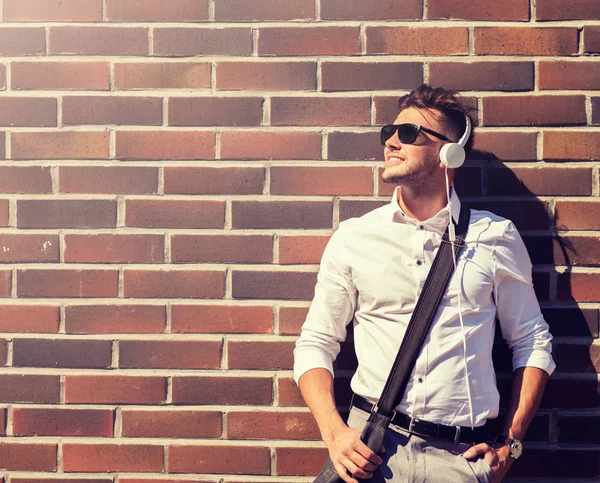 Joven en auriculares con bolsa sobre muro de ladrillo —  Fotos de Stock