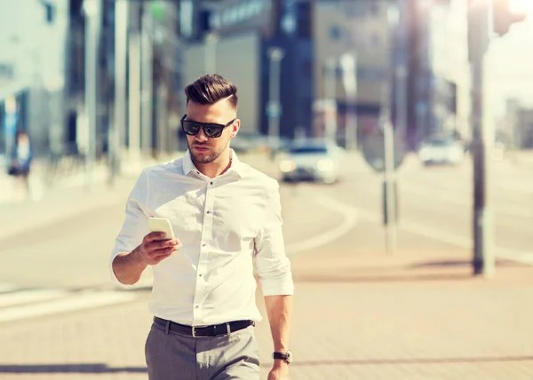 Людина в сонцезахисних окулярах зі смартфоном, що йде містом — стокове фото