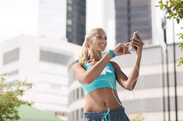 Lycklig kvinna med smartphone och hörlurar på stan — Stockfoto
