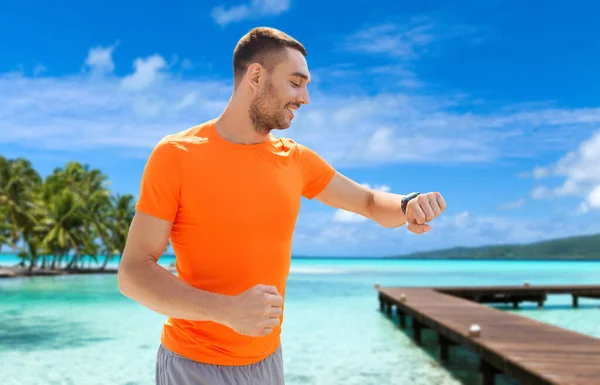Lächelnder Mann mit smarter Uhr läuft am Strand entlang — Stockfoto