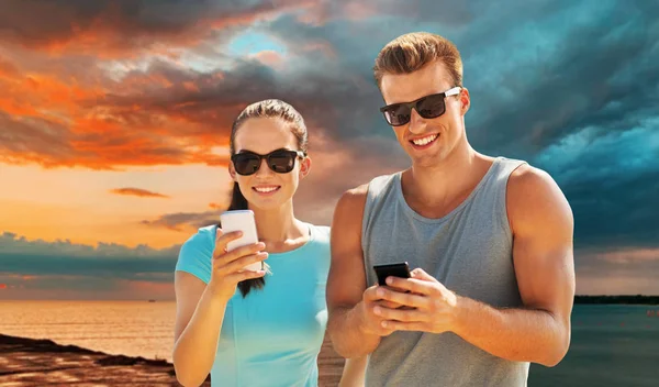 Couple en vêtements de sport avec smartphones sur la plage — Photo