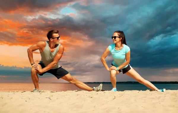 Sorridente coppia stretching gambe su spiaggia — Foto Stock