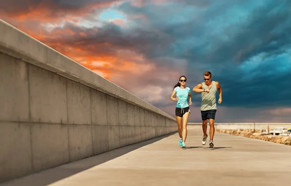 Koppel in sport kleding lopen langs pier — Stockfoto