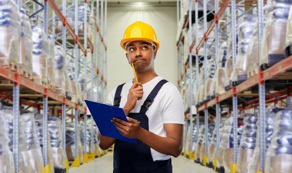 Thinking indian worker with clipboard at warehouse — Stock Photo, Image