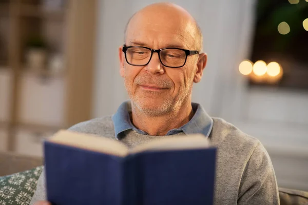 Heureux chauve senior homme sur canapé lecture livre à la maison — Photo