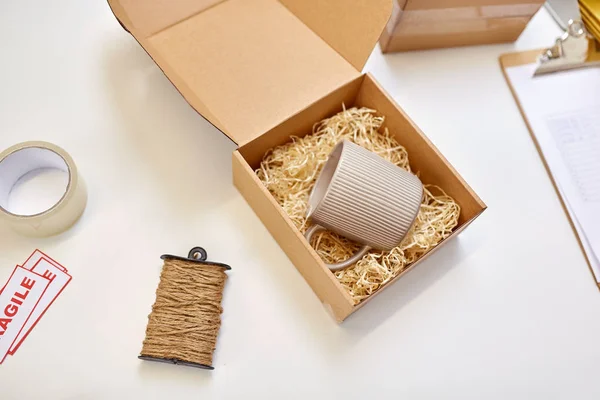 Paquete con relleno de paja y taza en la oficina de correos —  Fotos de Stock