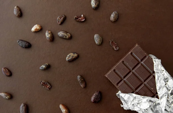 Dark chocolate bar in foil wrapper and cocoa beans — Stock Photo, Image