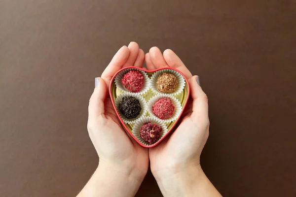 Руки з цукерками в шоколадній коробці у формі серця — стокове фото