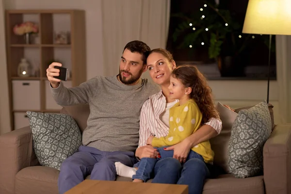 Família feliz levando selfie em casa à noite — Fotografia de Stock