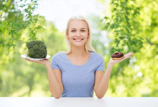 Femme souriante choisir entre brocoli et beignet — Photo