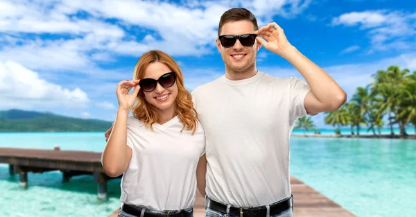 Happy couple in t-shirts and sunglasses on beach — Stock Photo, Image