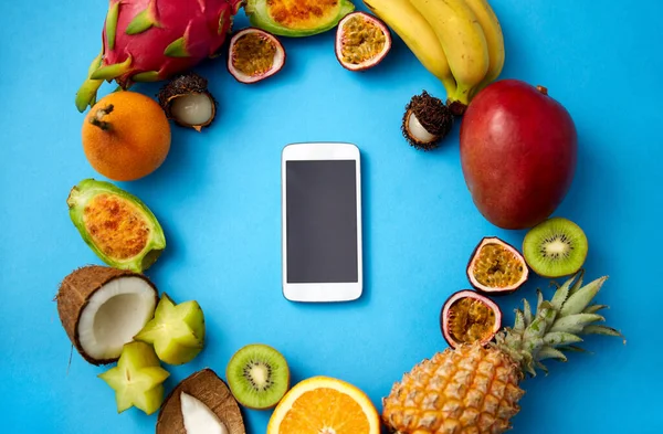 Exotic fruits around smartphone on blue background — Stock Photo, Image