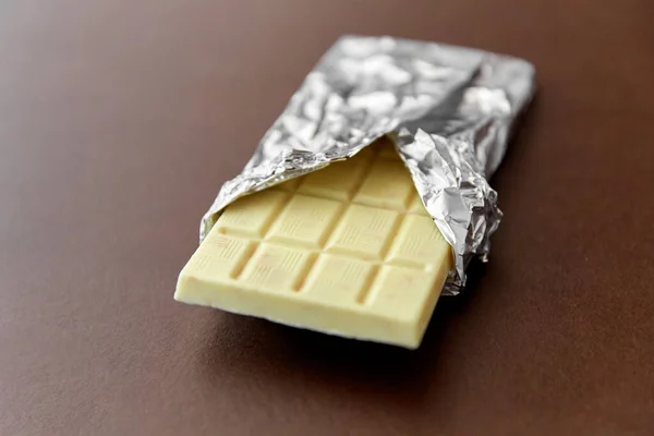 White chocolate bar in foil wrapper on brown — Stock Photo, Image