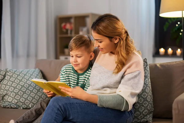 Happy mother and son reading book sofa at home — Stockfoto