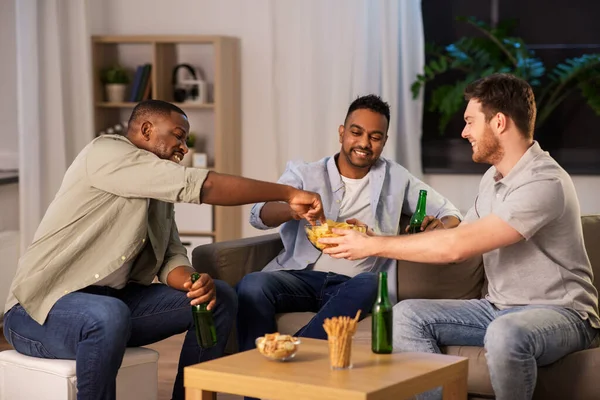 Amigos do sexo masculino beber cerveja com batatas fritas em casa — Fotografia de Stock