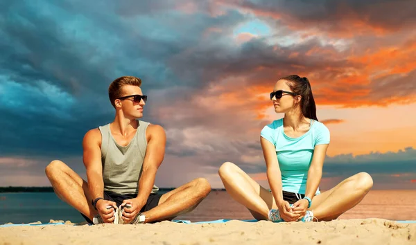 Sorrindo casal alongamento pernas na praia — Fotografia de Stock