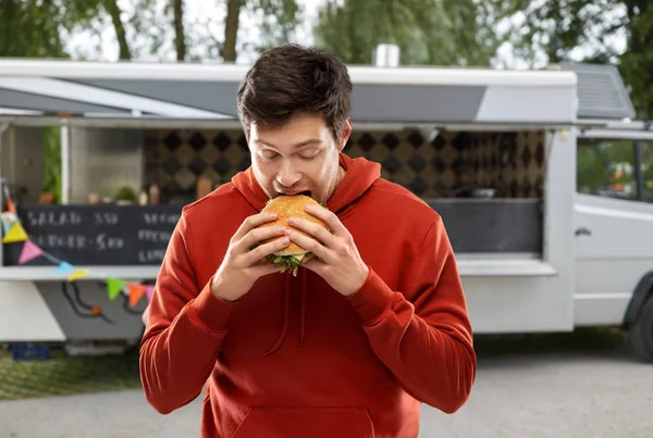 Голодний молодий чоловік їсть гамбургер у харчовій машині — стокове фото