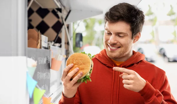 Jovem feliz mostrando hambúrguer no caminhão de comida — Fotografia de Stock