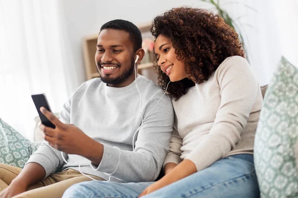 Casal feliz com smartphone e fones de ouvido em casa — Fotografia de Stock