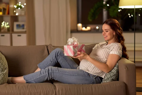 Счастливая улыбающаяся беременная женщина с подарочной коробкой дома — стоковое фото
