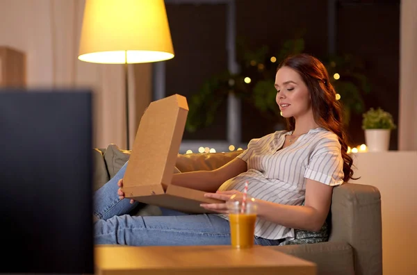 Donna incinta con scatola di pizza guardando la tv a casa — Foto Stock