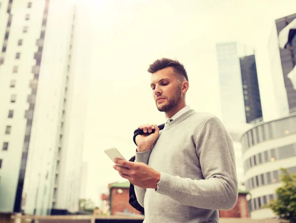 Young man with bag texting on smartphone in city — Stock Photo, Image