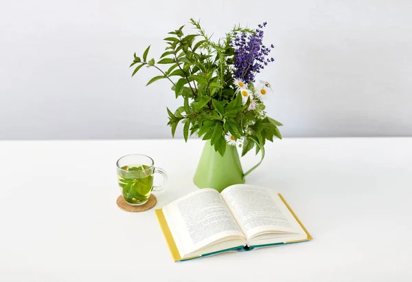 Örtte, bok och blommor i kannan på bordet — Stockfoto