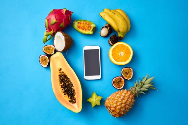 Frutas exóticas em torno do smartphone no fundo azul — Fotografia de Stock