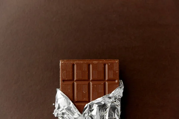 Chocolate bar in foil wrapper on brown background — Stock Photo, Image