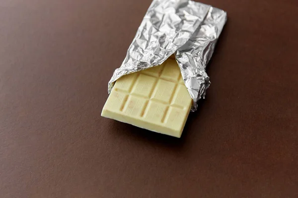 White chocolate bar in foil wrapper on brown — Stock Photo, Image