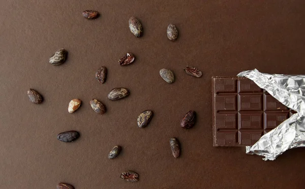 Coklat gelap bar dalam pembungkus kertas dan biji kakao — Stok Foto