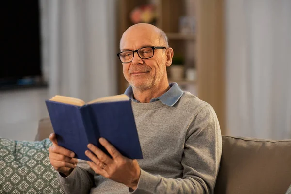 Ευτυχισμένος φαλακρός ηλικιωμένος άνδρας στον καναπέ διαβάζοντας βιβλίο στο σπίτι — Φωτογραφία Αρχείου