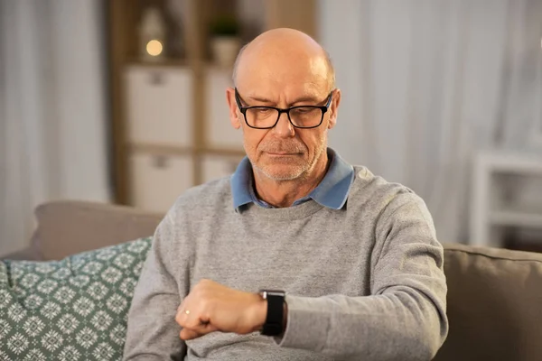Пенсионер смотрит на наручные часы дома — стоковое фото