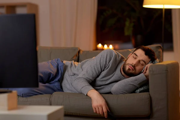 Homme dormant sur canapé avec télécommande TV à la maison — Photo