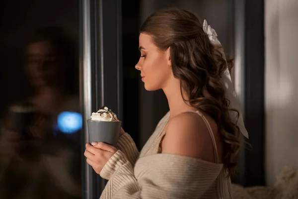 Mujer sosteniendo taza con crema batida en la noche —  Fotos de Stock