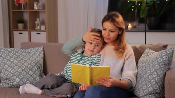 Happy mother and son reading book sofa at home — Stockvideo