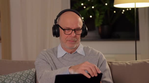 Senior man with tablet pc and headphones at home — Stock Video