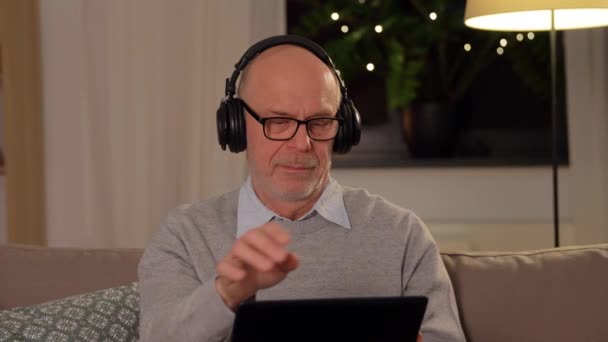 Homem idoso com tablet pc e fones de ouvido em casa — Vídeo de Stock