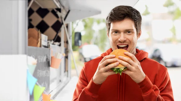 Jovem feliz comendo hambúrguer no caminhão de alimentos — Fotografia de Stock