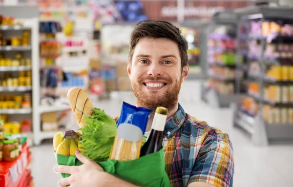 Uśmiechnięty młody człowiek z jedzeniem w torbie w supermarkecie — Zdjęcie stockowe
