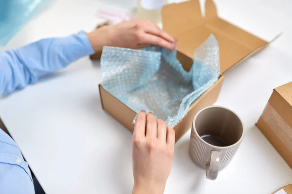 Hands packing mug to parcel box at post office — 스톡 사진