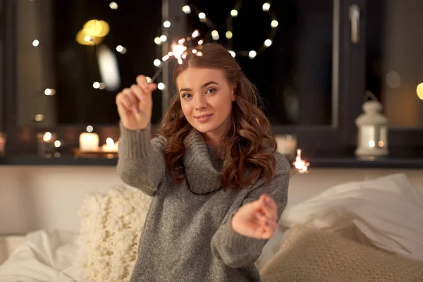 Happy young woman with sparklers in bed at home — Stock Photo, Image