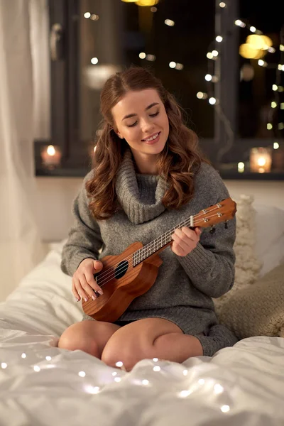 Felice giovane donna che suona la chitarra a letto a casa — Foto Stock