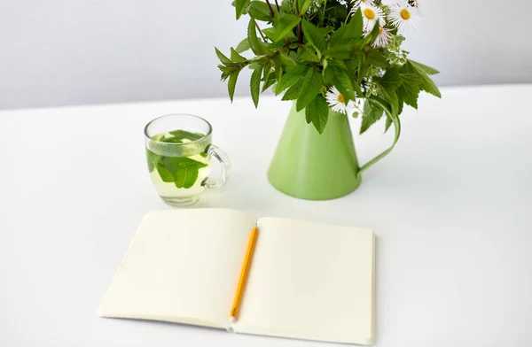 Chá de ervas, caderno e flores em jarro na mesa — Fotografia de Stock