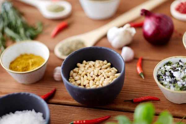 Pine nuts in bowl and spices on kitchen table — Stockfoto